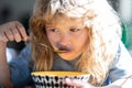 Cute child eats food itself with spoon. Little kid are eating soup, closeup kids face.