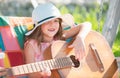 Cute child girl with blonde curly hair playing guitar on nature background. Happy cute teen girl swinging and having fun Royalty Free Stock Photo