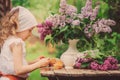 Cute child girl on cozy outdoor tea party in spring garden with bouquet of lilacs Royalty Free Stock Photo