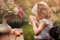 Cute child girl on cozy outdoor tea party in spring garden with bouquet of lilacs