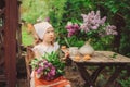 Cute child girl on cozy outdoor tea party in spring garden with bouquet of lilacs Royalty Free Stock Photo