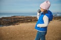 Cute child girl holds one hand in pocket, standing on the beach and drinking tea from a thermos cup, admiring the sea Royalty Free Stock Photo