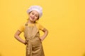 Cute child girl, little chef confectioner in apron and white chef cap, putting hands on waist, smiling looking at camera Royalty Free Stock Photo