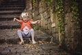Cute child girl in orange cardigan throwing leaves while sitting on stone road Royalty Free Stock Photo