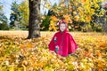 Cute child girl playing with fallen leaves in autumn