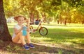 Cute child girl sit under the tree with bottle in hand. Bicycle