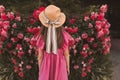 Cute child girl 5-6 year old wear straw hat with bow and summer dress posing with garden roses outdoors. Summer season. Royalty Free Stock Photo