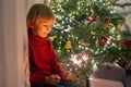 Cute child, holding sparkler at new year eve at home, sitting in front of the Christmas tree Royalty Free Stock Photo