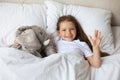 Cute child little girl wake up and lies in the bed with a toy elephant Royalty Free Stock Photo