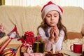 Cute child, lovely baby girl makes cherished wish, sitting by table with lit candle, surrounded by Christmas decorations Royalty Free Stock Photo