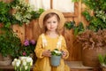 Cute child plays little gardener and plants flowers in a pot on porch of house. Little girl in straw hat and dress with potted flo Royalty Free Stock Photo