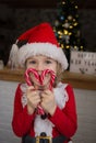 cute child in red santa hat, holding heart-shaped lollipops in front of his face Royalty Free Stock Photo