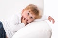 Cute child - shy girl lying on white sofa sucking thumb or finger Royalty Free Stock Photo