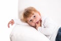 Cute child - shy girl lying on white sofa sucking thumb or finger Royalty Free Stock Photo