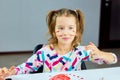 Cute child sitting at the table and drawing stripe camouflage on her face by hand Royalty Free Stock Photo