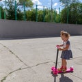 Cute child skilfully skates on a pink two-wheeled scooter on a s