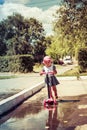 Cute child skilfully skates on a pink two-wheeled scooter on a s