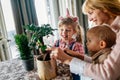 Cute children helping her mother to care for plants. Mom and her kids engaging in gardening at home.