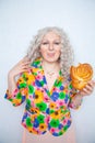 Cute chubby girl with white curly hair in a summer jacket with flowers holds a sweet pastry bun in the shape of a heart