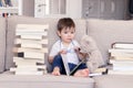 Cute clever funny little baby boy with thoughtful serious face expression holding glasses in hands reading book sitting on sofa wi Royalty Free Stock Photo