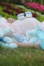 Cute composition with a pregnant young woman laying outdoors on the grass in the park surrounded by multiple baby stuffed toys and