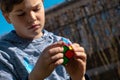 Cute concentrated boy playing rubik`s cube on the backyard. Young kid solving rubik`s cube Royalty Free Stock Photo