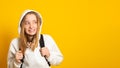 Cute cool schoolgirl dressed white hoodie on yellow background with backpack looking away. Banner