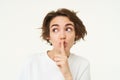 Cute and coquettish woman, keeps secret, gossips, holds finger on lips, shushing, hush gesture, stands over white Royalty Free Stock Photo