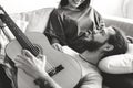 Cute couple on a couch boyfriend playing a guitar music and love concept