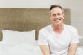 Man sitting on bed in bedroom with white duvet, pillows and beige headboard, copy space Royalty Free Stock Photo