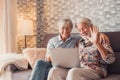 Cute couple of old people sitting on the sofa using laptop together shopping and surfing the net. Two mature people in the living Royalty Free Stock Photo