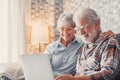 Cute couple of old people sitting on the sofa using laptop together shopping and surfing the net. Two mature people wearing