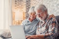 Cute couple of old people sitting on the sofa using laptop together shopping and surfing the net. Two mature people wearing