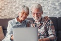 Cute couple of old people sitting on the sofa using laptop together shopping and surfing the net. Two mature people wearing Royalty Free Stock Photo