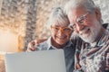 Cute couple of old people sitting on the sofa using laptop together shopping and surfing the net. Two mature people wearing Royalty Free Stock Photo