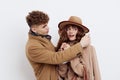 a cute couple is standing on a white background, wearing a coat. The man gently touches the ends of the woman& x27;s hat