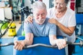 Cute couple of two seniros at the gym doing exercises - man holding a barr with weight witgh his wife helping him and looking it Royalty Free Stock Photo