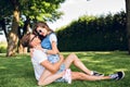 Cute couple of young people on grass in summer park. Pretty girl with long curly hair in shorts is sitting on handsome Royalty Free Stock Photo