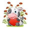 The cute cow with the little horn is sitting in the garden and holding the colored love doll