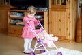 Cute crying baby girl making first steps with doll carriage. Royalty Free Stock Photo