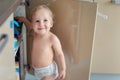 Cute curious caucasian baby boy open cupboard door in kitchen and exploring content. Funny toddler kid smiling and searching for