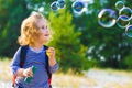 Horizontal portrait of a cheerful curly-haired girl with a red backpack and soap bubbles on a background of nature Royalty Free Stock Photo