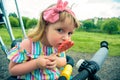 Cute curly baby girl eating watermelon candy in a sunny park. baby with outdoors lollipop Royalty Free Stock Photo