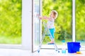 Cute curly girl washing a window in white room Royalty Free Stock Photo