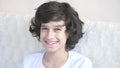 Cute curly-haired boy the teenager looks into the camera laughing and makes a funny facial expression. 4k, slow motion