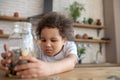 Cute curly-haired kid in a white tshirt holding a moneybank and looking unsatisfied Royalty Free Stock Photo