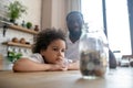 Cute curly-haired kid in a white tshirt looking at his moneybank and listening to his father Royalty Free Stock Photo