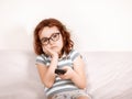 Cute curly little girl kid child in a eyeglasses bored watching tv at home with remote control in a hands Royalty Free Stock Photo