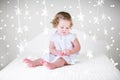 Cute curly toddler girl in a white dress on bed between Christmas lights Royalty Free Stock Photo