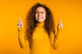 Cute curly young girl praying over yellow background. Woman begging someone. Royalty Free Stock Photo